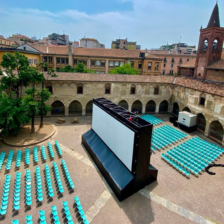 doppio-schermo Open-Air-Kino mit zwei Leinwänden in einem Kreuzgang mit hellblauen Stühlen